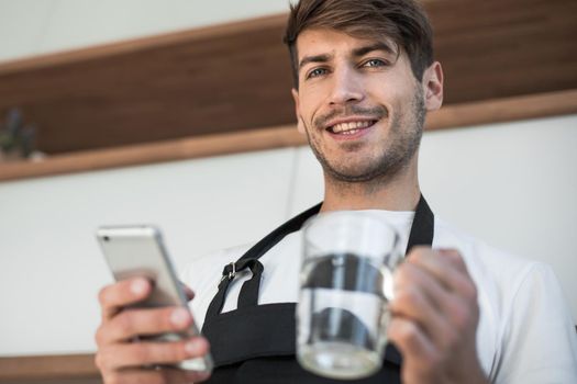 smiling young man with a smartphone standing in the kitchen.