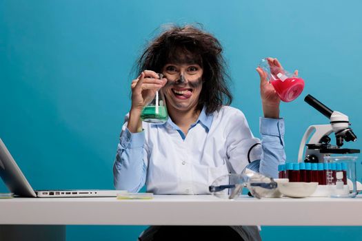 Foolish scientist with funny face expression handling beakers filled with serum.