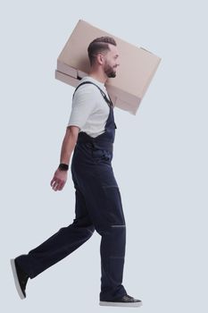 side view. a man in overalls carries a large cardboard box