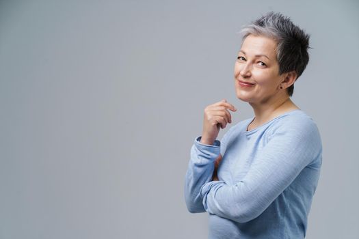 Lovely grey hair mature business woman in 50s posing sideways with hands folded and copy space on right isolated on white background. Copy space and place for product placement. Aged beauty