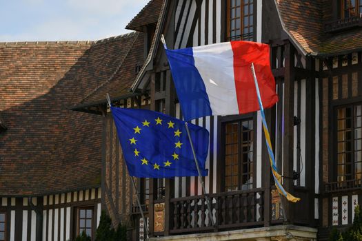 DEAUVILLE, FRANCE - APRIL 21, 2022 : The blue european flag with yellow stars and flag of France hanging on the city hall.