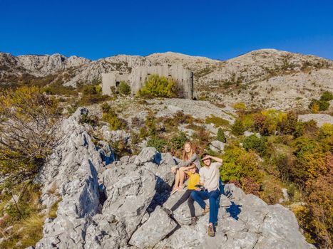 Happy family on the background of Collapsing tower of fortress Kosmac. Travel to Montenegro concept. Ancient Austro-Hungarian fortress built as a defensive structure and an observation post. Montenego