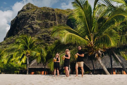 a stylish family in black clothes with coconuts in their hands on the beach of the island of Mauritius.Beautiful family on the island of Mauritius in the Indian ocean