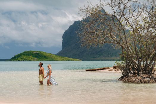 A girl in a swimsuit and a man in shorts stand in the ocean against the backdrop of mount Le Morne on the island of Mauritius.A couple in the water look into the distance of the ocean against the background of mount Le Morne Brabant