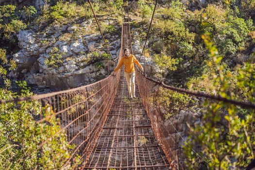 Man tourist on Old rusty bridge. Attraction Long extreme suspension iron bridge across the river Moraca. Sights of Montenegro. Landmark Montenegro