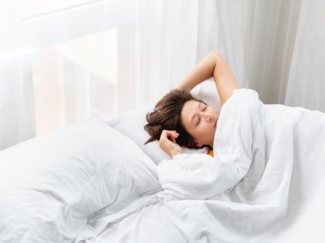 Caucasian woman is sleeping in bed. Healthy sleep on white bed linen. Morning at cozy home.