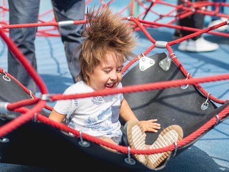 Laughing toddler is jumping on playground. Outdoor sport equipment for children physical development. Summer fun.