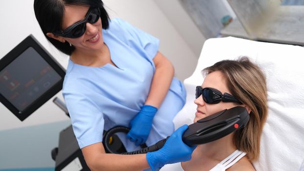 Beautician removing unwanted facial hair of client using laser in beauty salon