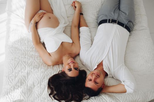 View from above of pregnant woman and husband lying on bed