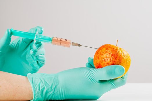 A hand in a medical glove inserts a syringe into apple. Harmful food additives. GMOs Concept