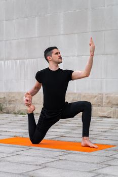 Handsome sporty latin man exercising in a city, doing yoga, sitting in variation of One Legged King Pigeon Pose.