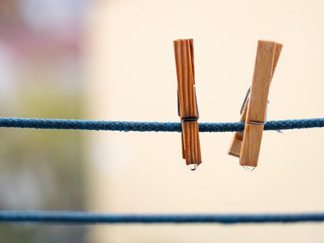 A pair of wooden clothespins on a blue rope with hanging waterdrops after the rain on blurred background.