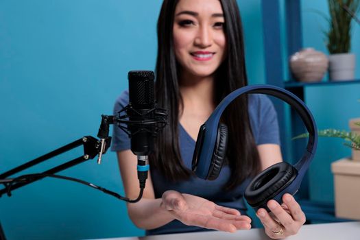 Asian vlogger creator holding headset talking into studio microphone