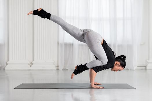 Asian woman working out in white hall, doing arm balancing handstand yoga asana, One Legged Crane Pose,