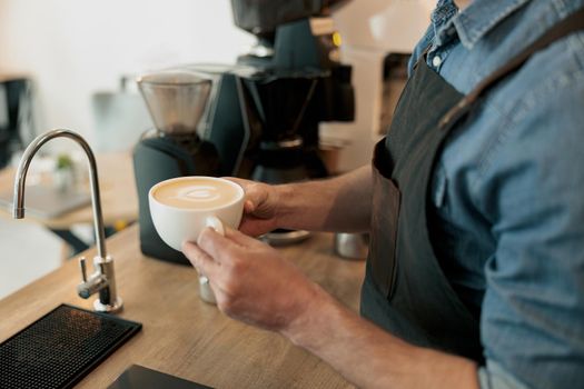 Barista hands holding white cup of coffee