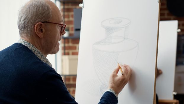Elder student using pencil to sketch vase model on paper