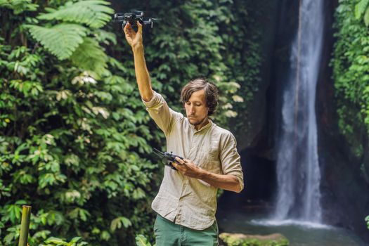 The man controls the drone against the background of the forest and the waterfall