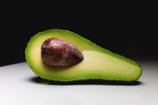 background. cut avocado in half, with a bone inside, lies on the table. view from above