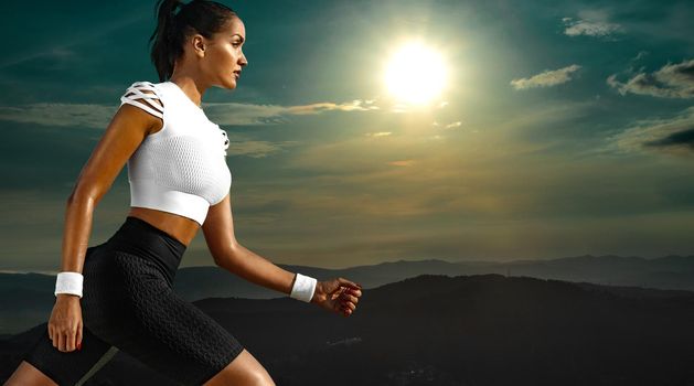 Sporty young woman and fit athlete runner running on the sky background in the mountains. The concept of a healthy lifestyle and sport. Woman in black and white sportswear.