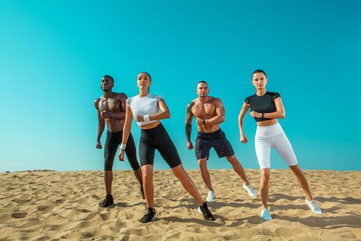 Group of young sportsmens women and men, fit athletes runners running on the sky background. Healthy lifestyle and sport. Friends in black and white sportswear on workout exercise. Fitness concept.