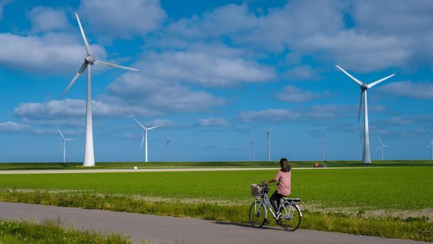 young woman electric green bike bicycle by windmill farm , windmills isolated on a beautiful bright day Netherlands Flevoland Noordoostpolder