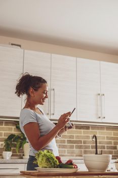 A young woman in the kitchen holds a tablet in her hands communicating in a chat