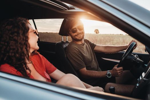 Cheerful Man and Curly Brunette Woman Sitting in the Car, Young Couple Enjoying Road Trip at Sunset