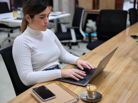 woman in a workspace using her computer with a coffee next to it