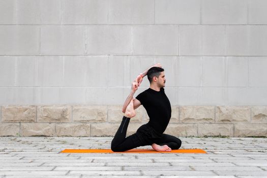 Handsome latin man doing yoga in a city. One Legged King Pigeon Pose.