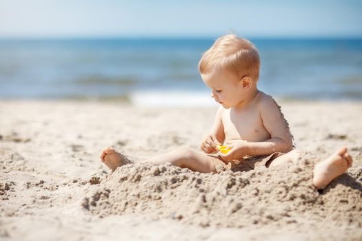 Boy toddler is playing with sand on beach