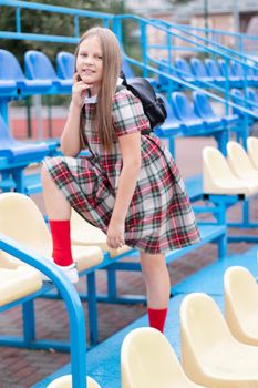 pretty girl in school dress uniform on the blue and yellow tribune of the school stadium. school time. tween.