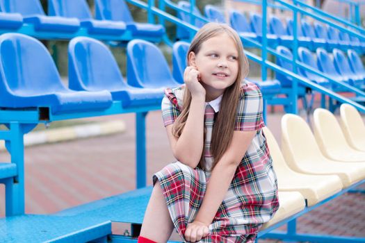 pretty girl in school dress uniform on the blue and yellow tribune of the school stadium. school time. tween.