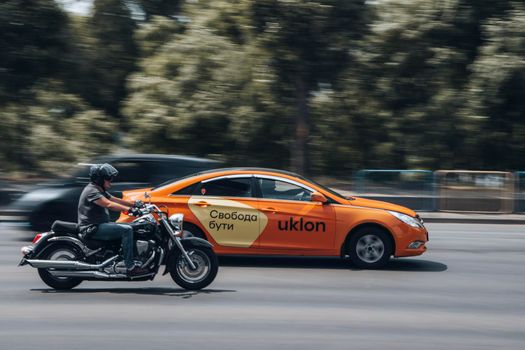 Ukraine, Kyiv - 27 June 2021: Orange Chevrolet Epica Uklon Taxi cat and Suzuki Intruder motorcycle moving on the street. Editorial