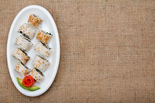 Uramaki sushi rolls with avocado and red fish on ceramic plate.