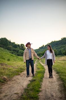 A Caucasian heterosexual couple walks down the alley, holding hands, near a picturesque village in Ukraine. Vertical photo.
