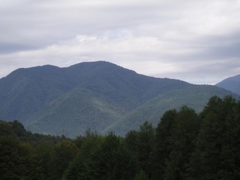 A panorama mountain landscape with valleys and forest mountain peaks under an overcast and cloudy sky