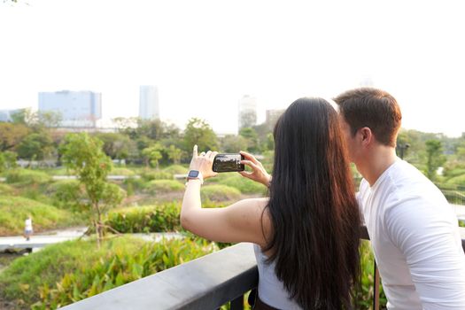 Couple taking photos of the cityscape with the mobile from a park at sunset
