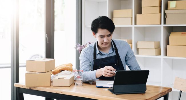 Asian business men use laptop computer checking customer order online shipping boxes at home. Starting Small business entrepreneur SME freelance. Online business, Work at home concept.