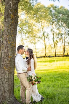 Happy young couple in green wheat field on their wedding day. Smiling newlyweds walking in the nature, holding hands. Family life, wedding concept.