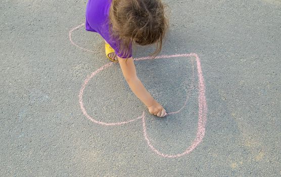 the child paints chalk on the asphalt heart. Selective focus.