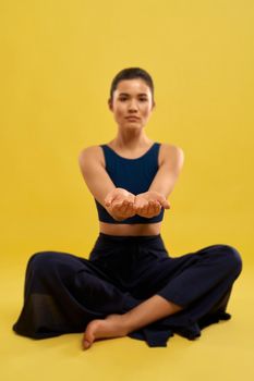 Woman sitting in easy pose of yoga, stretching arms forward indoors.