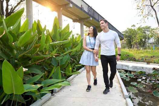 Multiethnic couple walking distracted for a path of an urban park during sunset