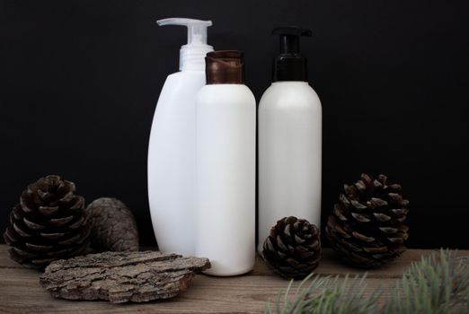 Mockups of a white plastic cosmetic bottles with a dispenser on a black background with tree bark and fir cones