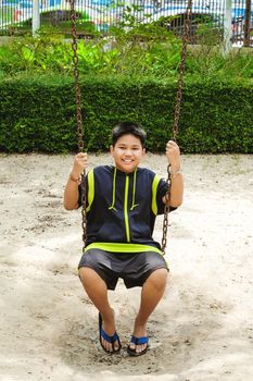 Happy asian sport boy play on swing playground in Garden.