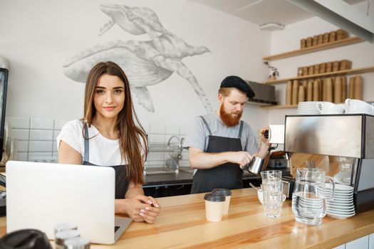 Coffee Business Concept - Positive young bearded man and beautiful attractive lady barista couple enjoy working together at the modern coffee shop