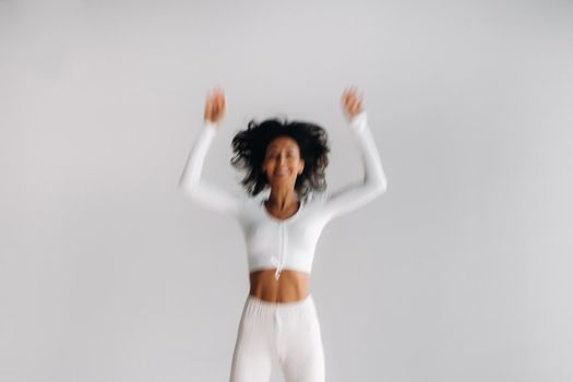 A blurry silhouette of a woman in white sportswear bounces on a white background. The girl, jumping, raised her hands up in the gym.