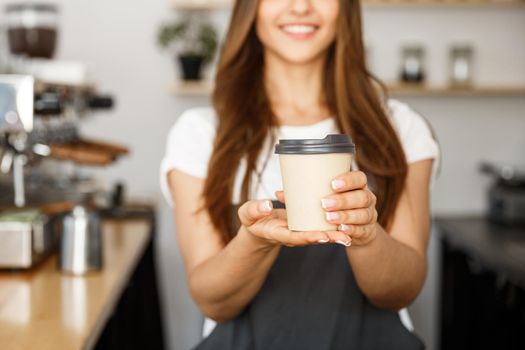 Coffee Business Concept - Beautiful Caucasian lady smiling at camera offers disposable take away hot coffee at the modern coffee shop