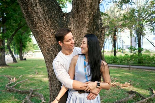 Close up portrait of a multiethnic newly married couple embracing next to a tree
