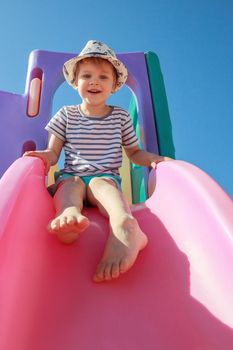 Happy child playing with pink slide on blue sky background. Playtime concept.
