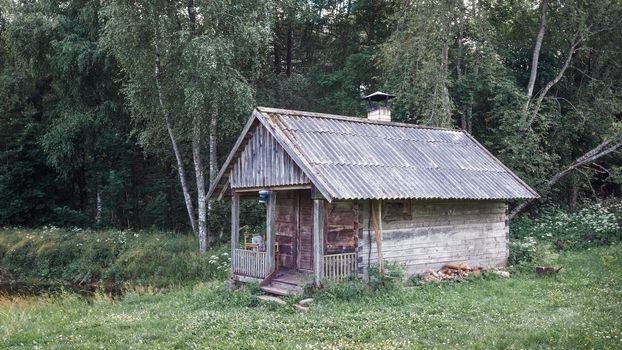 Old and abandoned bathhouse near the pond in meadow, country forest, Lithuania
